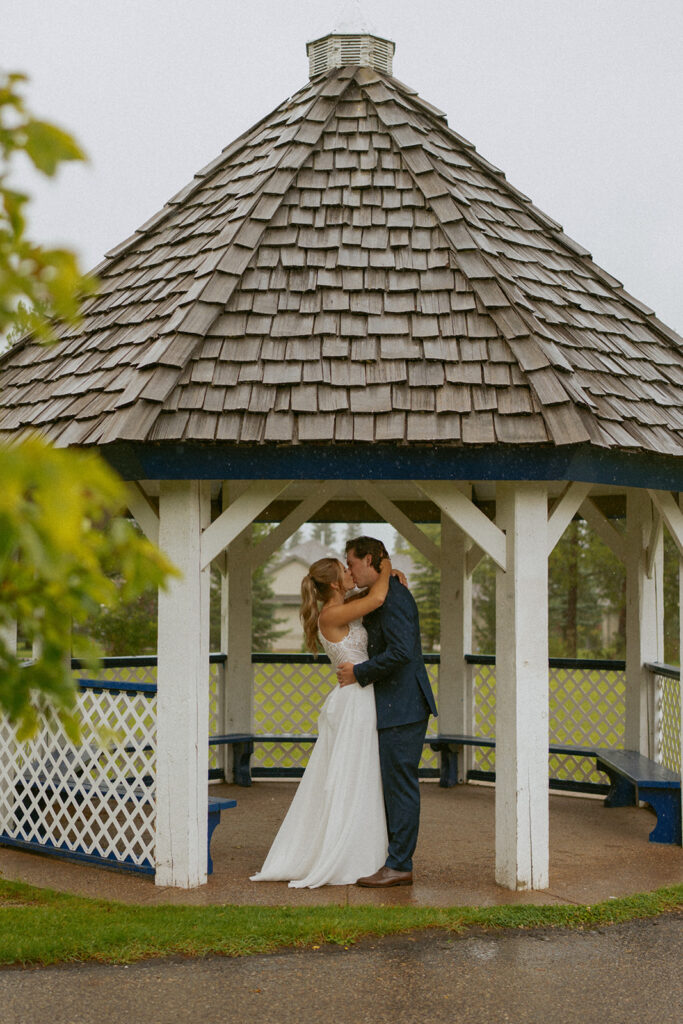 Edson Alberta Wedding Photographer, Bride and Groom Kiss in a white gazebo in the rain