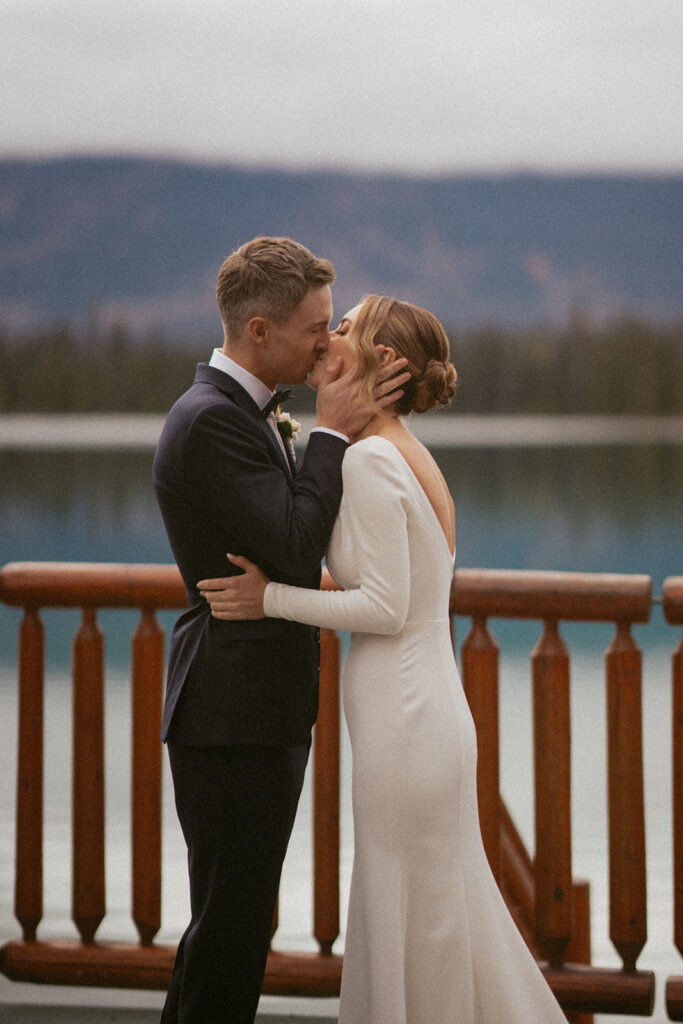 First kiss bride and groom at Fairmont Jasper Park Lodge overlooking the water