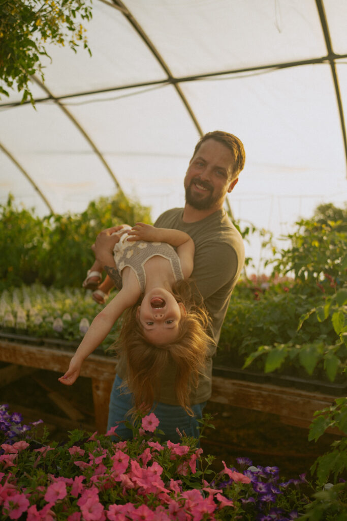 silly photo of father holding daughter in the air for a photo in a greenhouse