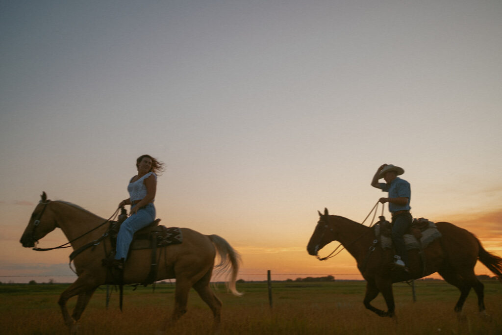 couple riding their horses through a field at sunset in alberta