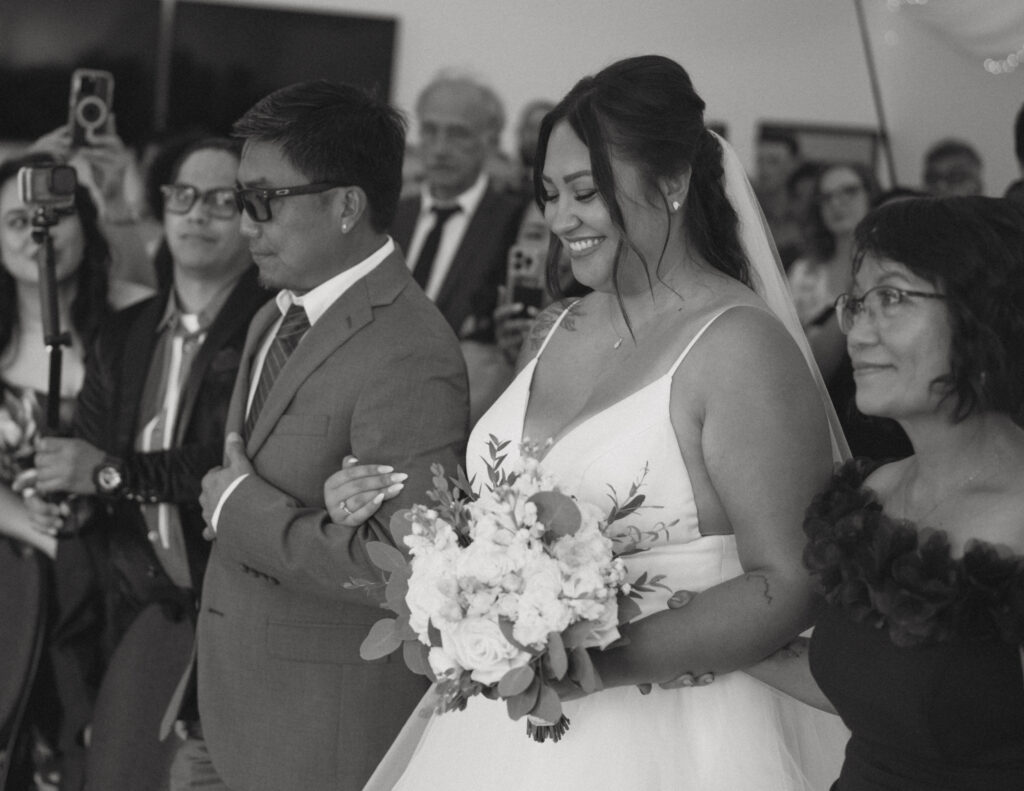 Bride entering the ceremony arm in arm with her parents at a Hinton Alberta wedding.