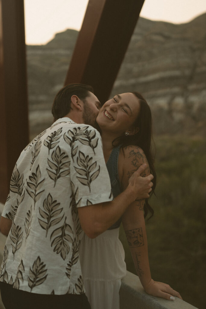 Couple sharing a playful moment on a bridge at sunset, captured by a Drumheller wedding photographer.