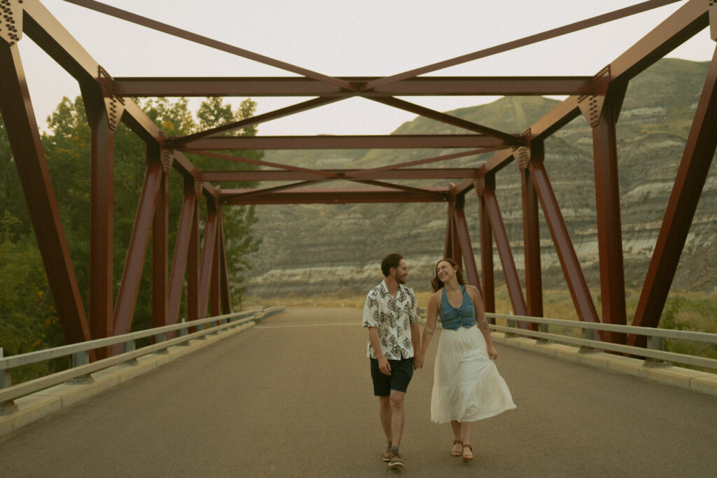 Couple sharing a playful moment on a bridge at sunset, captured by a Drumheller wedding photographer.