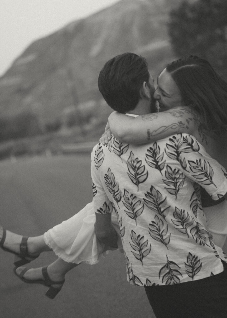Couple sharing a playful moment on a bridge at sunset, captured by a Drumheller wedding photographer.