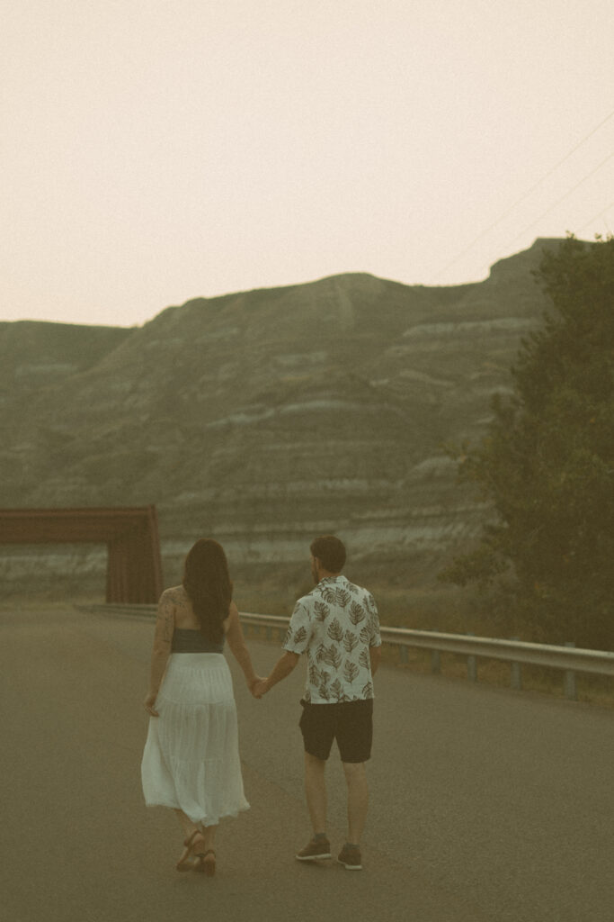 Couple sharing a playful moment on a bridge at sunset, captured by a Drumheller wedding photographer.
