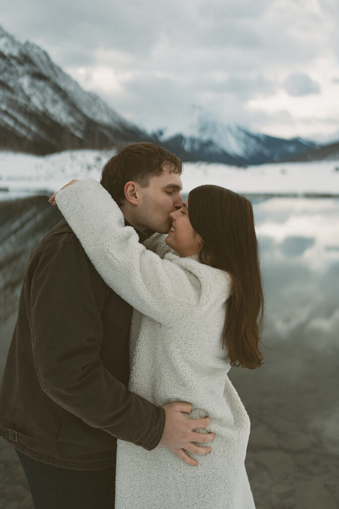 Couple embracing in soft snowfall during mountain engagement session