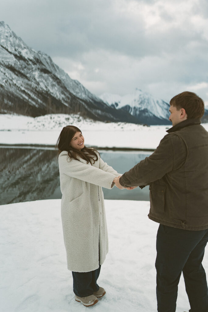 Candid engagement photos of couple exploring snowy lakeshore in Jasper
