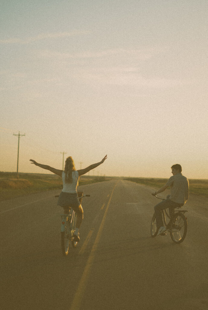 Young couple laughing together while riding bikes during a storytelling engagement session in Lloydminster.
