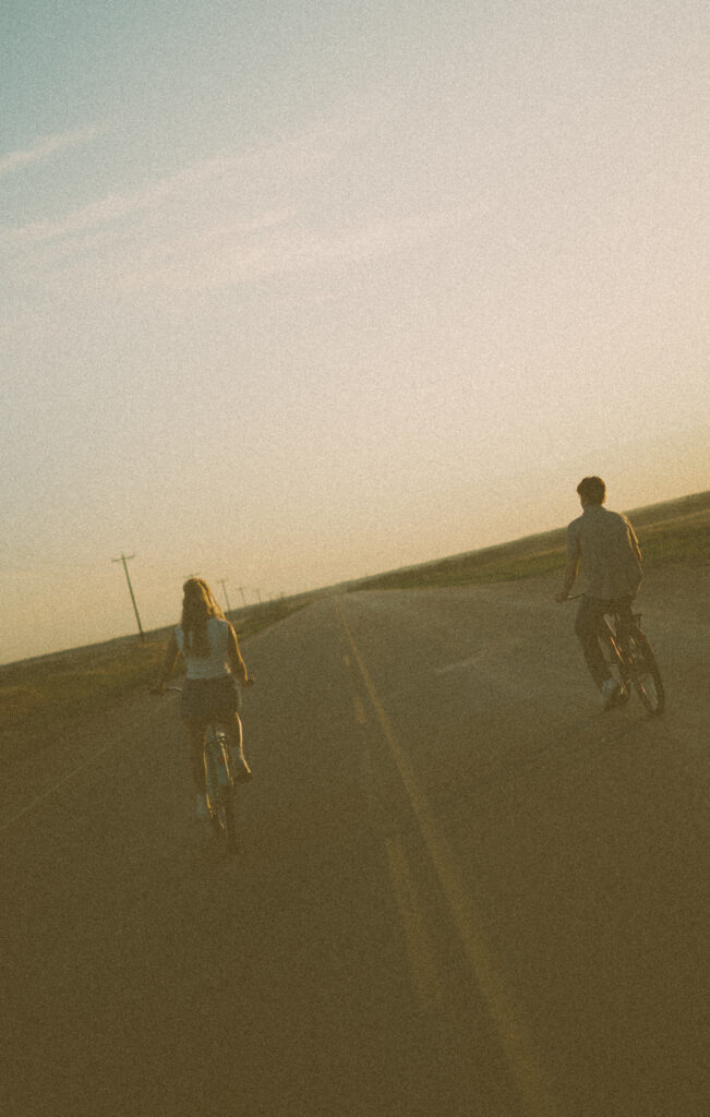 Young couple laughing together while riding bikes during a storytelling engagement session in Lloydminster.