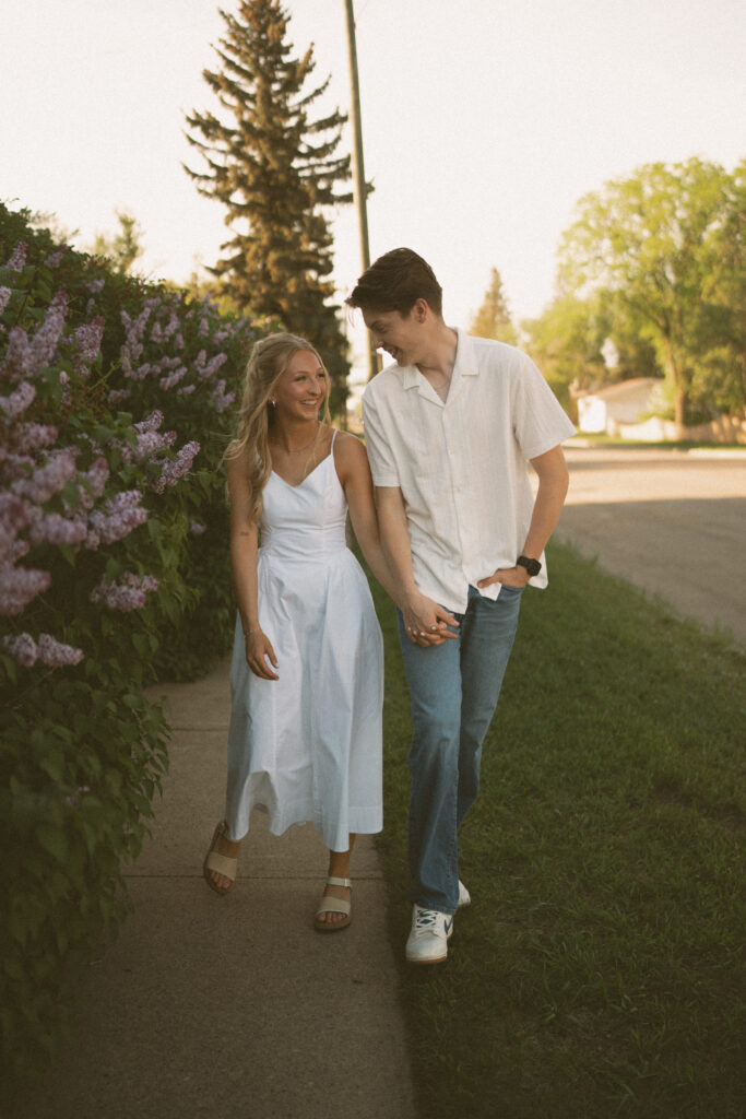 Playful engagement photo of a couple walking through a tree-lined neighborhood in Lloydminster.