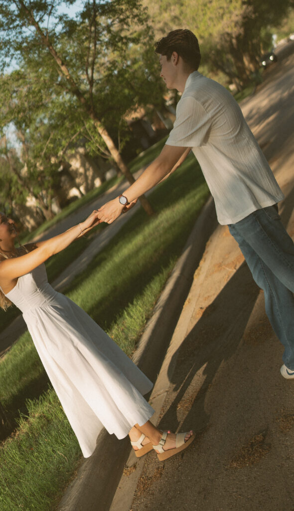 Playful engagement photo of a couple walking through a tree-lined neighborhood in Lloydminster.