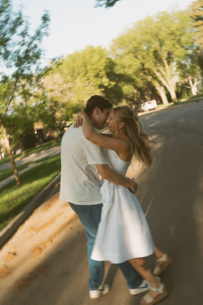 Playful engagement photo of a couple walking through a tree-lined neighborhood in Lloydminster.