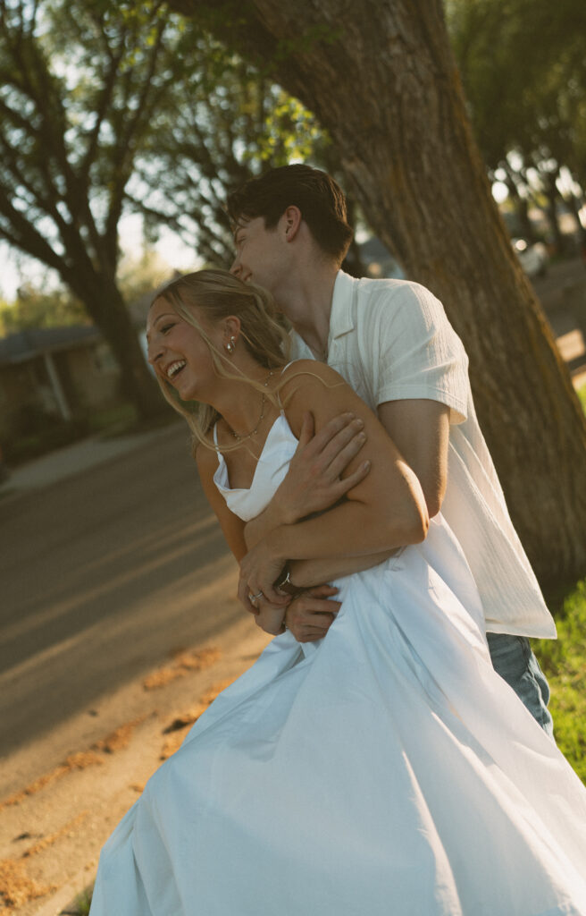Playful engagement photo of a couple walking through a tree-lined neighborhood in Lloydminster.