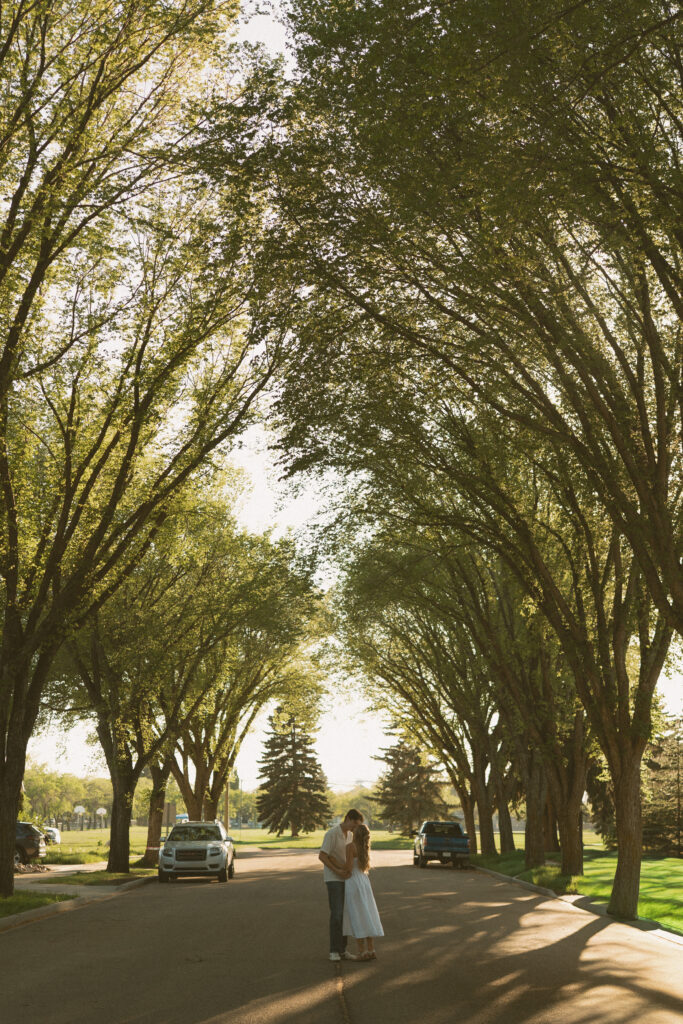 Playful engagement photo of a couple walking through a tree-lined neighborhood in Lloydminster.