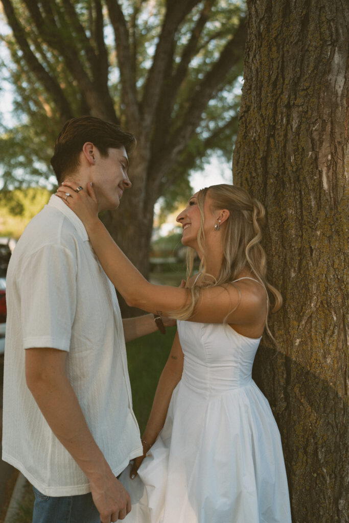 Playful engagement photo of a couple walking through a tree-lined neighborhood in Lloydminster.