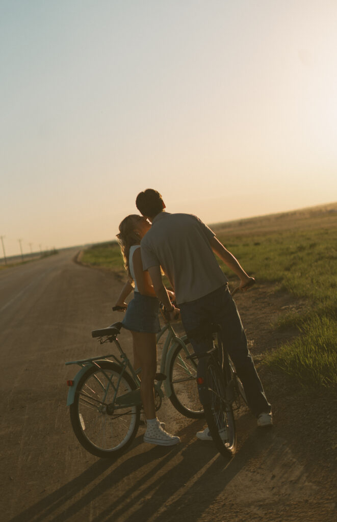 Young couple laughing together while riding bikes during a storytelling engagement session in Lloydminster.