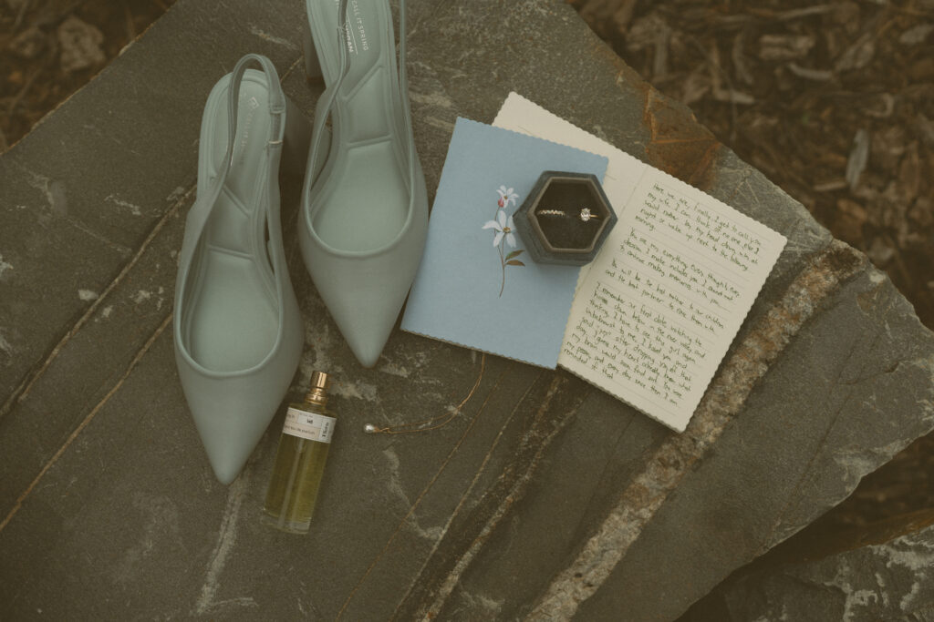 Wedding invitation suite, rings, blue bridal shoes, and stationery photographed on stone at Fairmont Jasper Park Lodge.